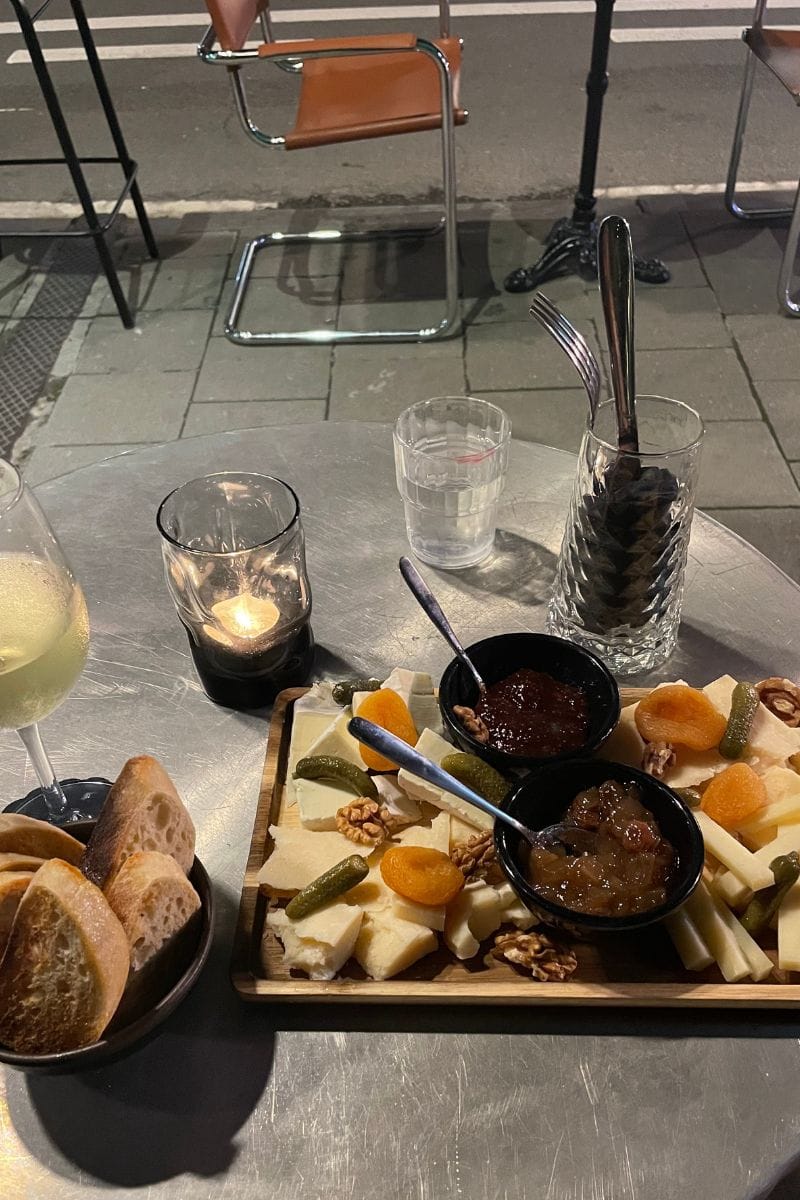 A cheese platter and toasted sliced baguettes, on a metal table, by the road