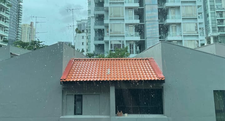 A photo of a view outside a window on a rainy day with grey skies, and a bright red rooftop